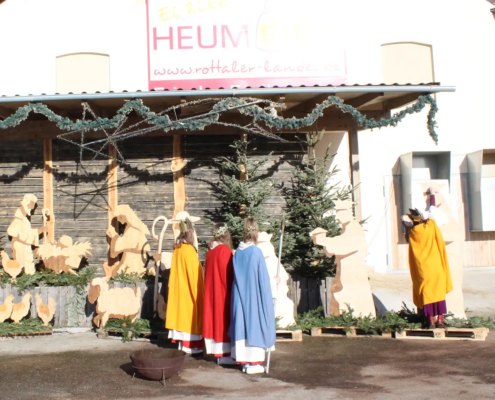 Kinder in Kostümen der heiligen drei Könige vor einer Krippe am Heumeierhof