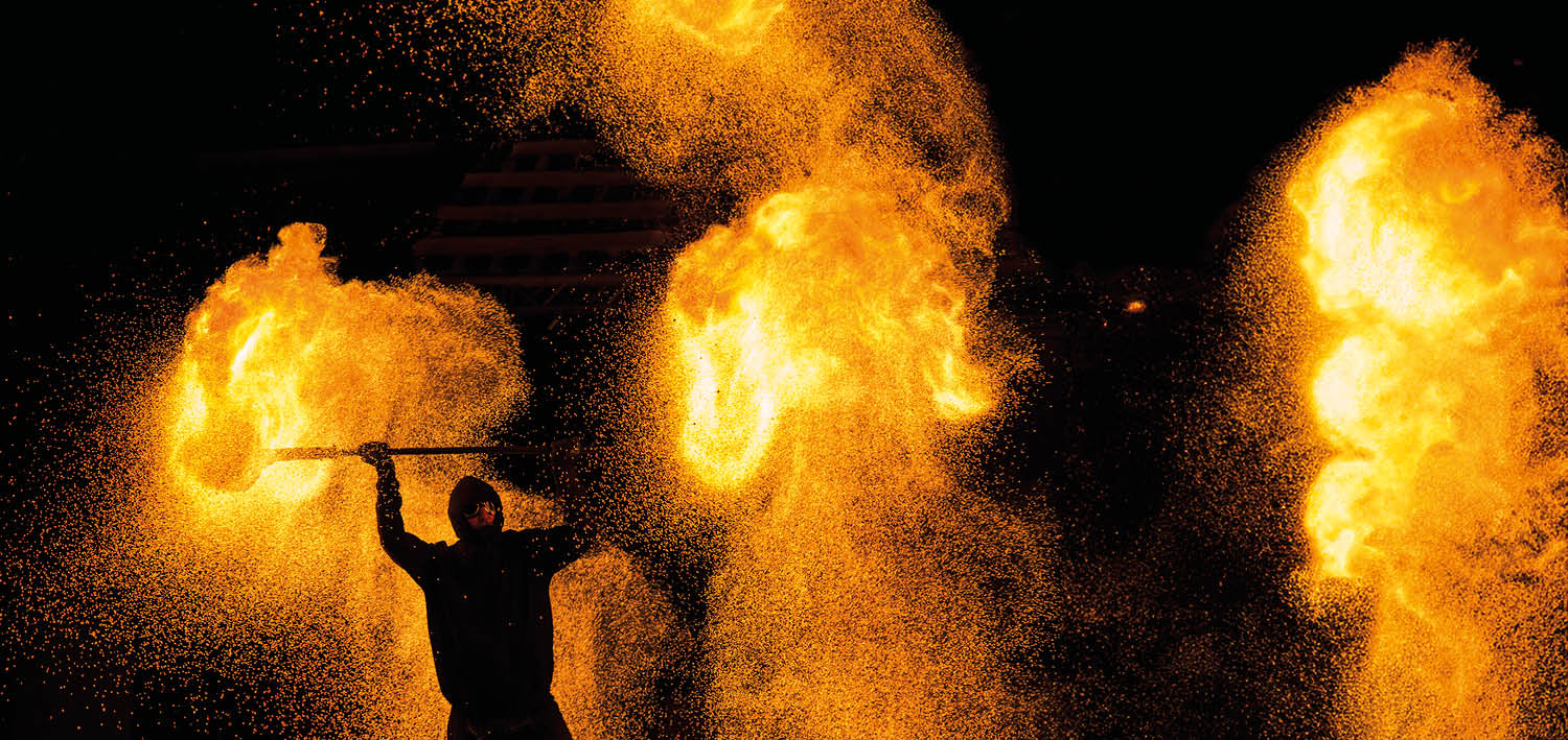 Ein Mann absolivert eine Feuershow, Wolken aus Glut färben das Szenario